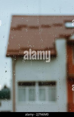 Gouttes de pluie sur une fenêtre le jour d'automne froid. Vue sur le toit d'un immeuble d'appartements dans Defocus. Sombre saison pluvieuse automne. Dépose la texture sur une surface Banque D'Images