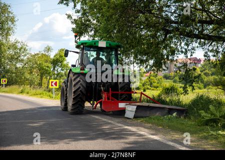 Grand tracteur industriel moderne coupant de l'herbe verte avec un équipement de tonte le long des routes de campagne. Route machine de tondeuse à gazon véhicule autoroute Banque D'Images