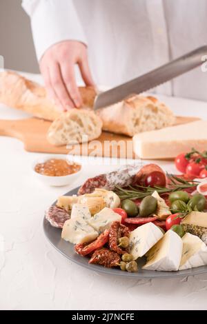 Femme servant des antipasti italiens traditionnels sur une table blanche. Assiette de charcuterie avec différents types de saucisses et fromages - salami, dorblu, prostcuitt Banque D'Images