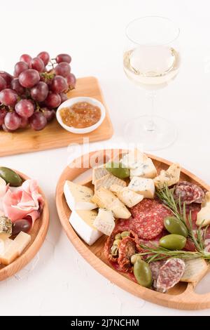 Composition verticale avec assiette d'antipasti - variété de fromages, saucisses servies avec un verre de vin, tomates séchées au soleil, olives, confitures et herbes sur la merche Banque D'Images