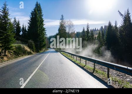 Route dans les montagnes des Carpates ukrainiens. Piste et brouillard réchauffés par le soleil, par évaporation après la pluie. Belle vue sur les sapins et autres arbres. Banque D'Images