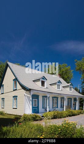 Vieux 1810 jaune avec des bordures blanches et bleues maison de style Canadiana avec cour avant paysagée en été. Banque D'Images