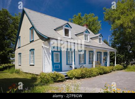 Vieux 1810 jaune avec des bordures blanches et bleues maison de style Canadiana avec cour avant paysagée en été. Banque D'Images