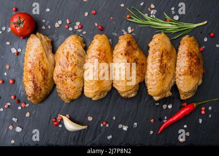 Ailes de poulet avec sauce barbecue, poivre chaud, tomate sur un tableau noir Banque D'Images