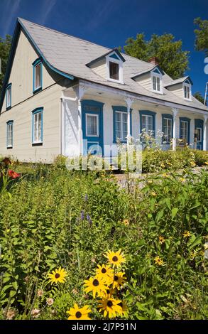 Vieux 1810 jaune avec des bordures blanches et bleues maison de style Canadiana avec cour avant paysagée en été. Banque D'Images