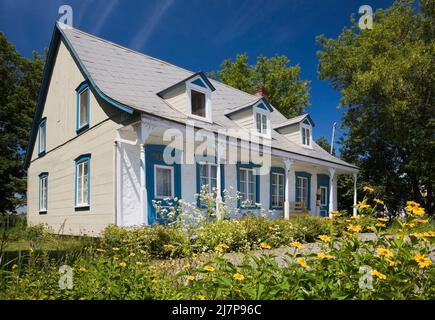 Vieux 1810 jaune avec des bordures blanches et bleues maison de style Canadiana avec cour avant paysagée en été. Banque D'Images