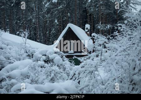 Maison dans village en hiver. Il y a beaucoup de neige sur le toit de la vieille maison. Vue sur le village en forêt. Banque D'Images