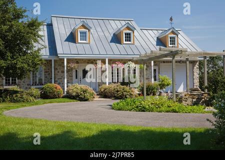 Réplique de l'ancienne maison en pierre de campagne de style cottage Canadiana 1800s avec garniture blanche et toit en tôle d'argent en été. Banque D'Images