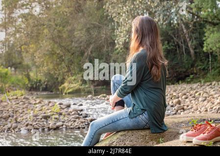 Femme assise sur un rocher tenant sa jambe. Femme se détendant dans la nature Banque D'Images