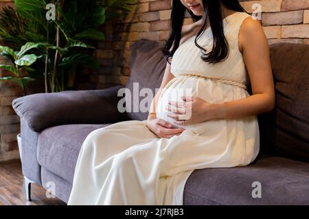 Close-up of young pregnant woman touching maternité et la tenue d'un enfant à naître à l'intérieur du ventre est assis sur un canapé à la maison Banque D'Images