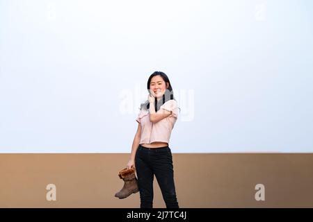 Une femme asiatique tient des bottes brunes dans la main et l'affiche pour le tournage de photos sur le toit à l'heure du crépuscule. Banque D'Images