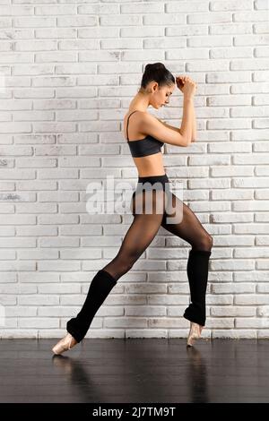 Vue latérale du corps entier de la ballerine FIT dans les chaussures d'activewear et pointe debout sur les pieds de pied à pied près du mur de briques blanches dans le studio Banque D'Images