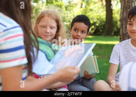 Enseignant lisant le livre à ses petits élèves dans le parc Banque D'Images