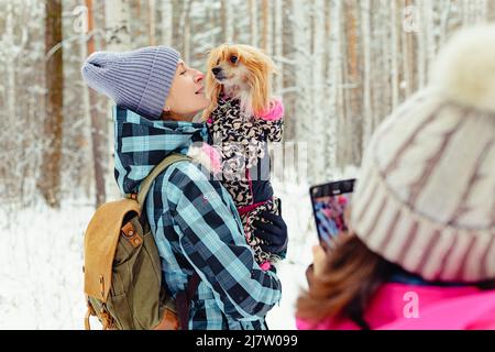 Un adolescent prend une photo sur un smartphone de maman et de chien. Une femme tient un chien chinois Crested dans ses bras. Promenades en famille en plein air en hiver Banque D'Images