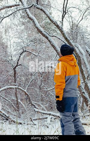 Un homme d'âge moyen marche dans la forêt d'hiver. Combinaisons sport d'hiver. Promenez-vous dans le parc à l'extérieur. Vue arrière. Tir vertical Banque D'Images