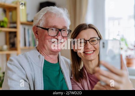 Fille adulte rendant visite à son père senior à la maison et prenant le selfie. Banque D'Images
