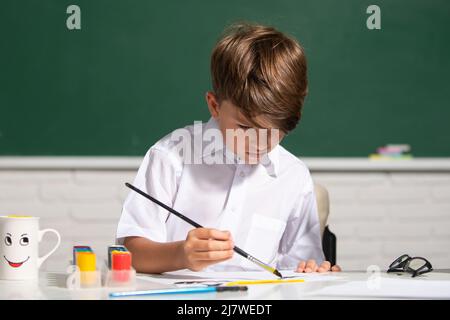 Joli petit enfant dessin en classe. Portrait d'un garçon d'école qui apprécie la leçon d'art et d'artisanat à l'école. Apprentissage de l'enfance, compétences en matière d'statistique pour les enfants. Banque D'Images