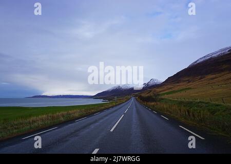 Route vide à côté de la mer, avec des montagnes et des champs enneigés, sur le périphérique dans le nord de l'Islande Banque D'Images