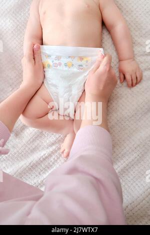 Une mère femme met une couche pour un bébé garçon. Maman habille l'enfant dans des vêtements sur le lit. Banque D'Images