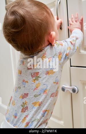 Bébé garçon se déporte d'un tiroir de cabinet avec sa main. L'enfant tient la poignée de la porte de l'armoire, petit enfant Banque D'Images