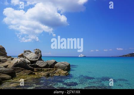 Une carte postale bleue de l'île de Mykonos: La mer Méditerranée calme à Platis Gialos, avec yacht, ciel bleu et nuages blancs Banque D'Images