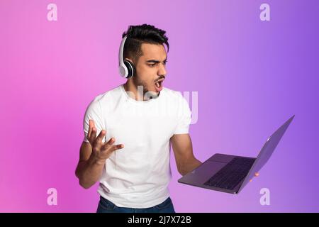 Un jeune arabe en colère dans un casque criant sur un ordinateur portable, se sentant frustré, manquant la date limite du projet de travail Banque D'Images