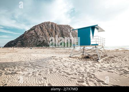 Blue Lifeguard Stand à Morro Beach pendant le coucher du soleil en Californie avec Morro Rock au loin Banque D'Images