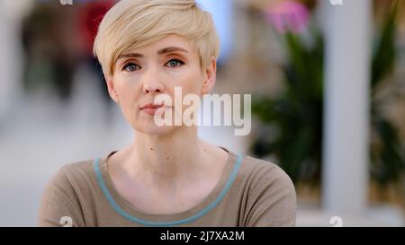 Portrait d'intérieur de femme belle femme mûre d'âge moyen blonde avec les cheveux courts froissés et le maquillage naturel regarde en distance se transforme en caméra calme Banque D'Images
