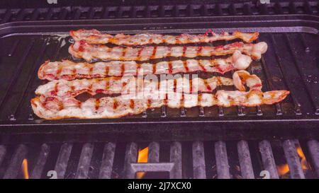 Cuisson de tranches de bacon sur un barbecue à gaz extérieur. Banque D'Images