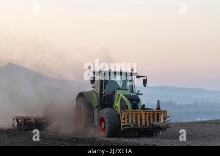 Un tracteur Claas Axion 850 génère des nuages de poussière lorsqu'il fait surpasser une herse à disques sur un champ labouré à Dusk, dans la campagne de l'Aberdeenshire Banque D'Images