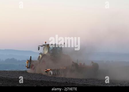 Nuages de poussière produits par un tracteur remorquant une herse à disques sur un champ labouré tard dans la soirée Banque D'Images