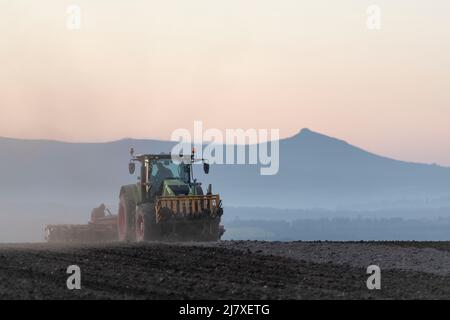 Un tracteur Claas tractant une herse à disques au-dessus d'un champ labouré dans la soirée à Aberdeenshire avec Bennachie visible au loin Banque D'Images