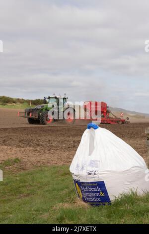 Un tracteur Fendt et un semoir Horsch fonctionnant dans un champ labouré à Aberdeenshire, avec un sac de semences du commerçant assis à l'entrée du champ Banque D'Images