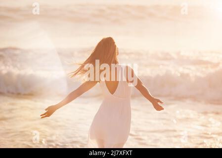 une jeune femme appréciant son temps à la plage. Femme insouciante profitant du soleil sur la plage. Retour d'une femme de contenu insouciante célébrant et appréciant Banque D'Images