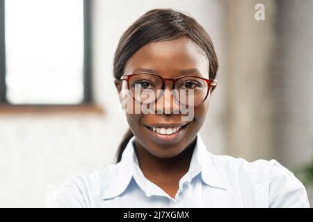 Portrait en gros plan de charmante femme d'affaires afro-américaine positive portant des lunettes élégantes et une chemise habillée. Une employée de bureau confiante regarde la caméra. Banque D'Images