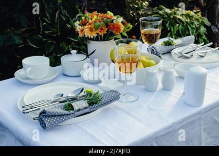 Table pour manger à l'extérieur sur une table dans le jardin. Table élégante avec vaisselle blanche sur nappe blanche. Lumière du jour ensoleillée. Copier la flèche Banque D'Images
