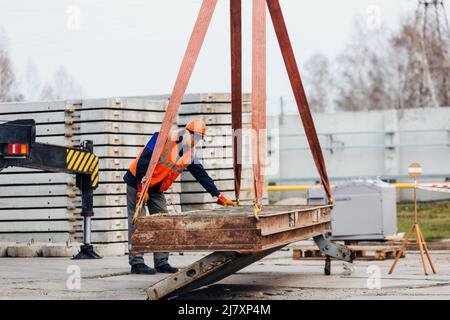 L'aiguillon dans le casque et le gilet contrôle le déchargement des structures métalliques sur le chantier de construction. Le handyman blanc décharge la charge. Banque D'Images