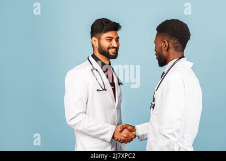 portrait de przloseup d'un professionnel de la santé intellectuel avec un laque blanc discutant des résultats avec un jeune médecin sur fond bleu Banque D'Images