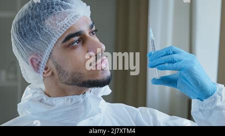 Jeune arabe homme hispanique médecin praticien chirurgien dans l'uniforme médical de protection spécial porte des gants en caoutchouc tient la seringue avec le vaccin de médecine Banque D'Images