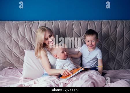 Famille s'amusant ensemble le week-end ensemble.mère et deux enfants au lit. Mère blonde et bébé garçons jouant dans la chambre du matin. Parent et petit Banque D'Images