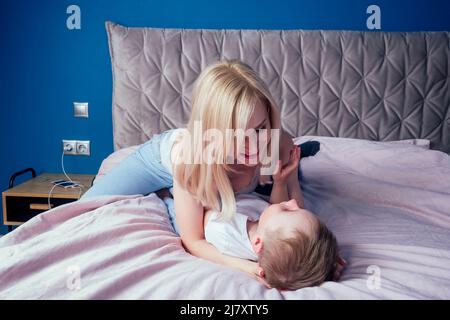 Famille s'amusant ensemble le week-end ensemble.mère et deux enfants au lit. Mère blonde et bébé garçons jouant dans la chambre du matin. Parent et petit Banque D'Images