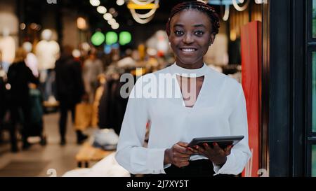 Portrait Afro-américain heureux souriant heureux réussi vendeur femme consultant dans le magasin de vêtements commerçant employé de boutique tenant numérique Banque D'Images