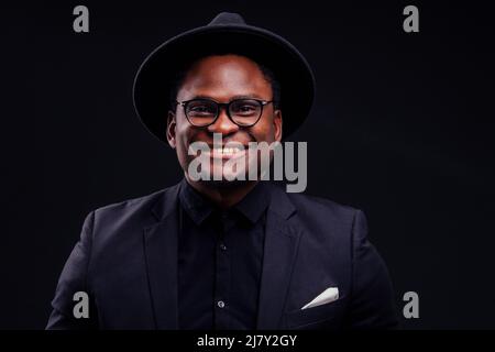 jeune beau afro-américain mélancolie garçon dans une veste et des lunettes sur un fond noir dans le studio.mystère et chagrin se cachent Banque D'Images