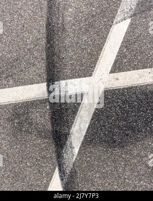 Image détaillée d'une marque de pneu en caoutchouc noir sur des lignes peintes en blanc dans un stationnement Banque D'Images