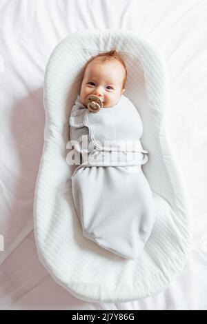 Mignon blanc blanc bébé de deux mois couché dans cocon à la maison et sucer mamelon. Banque D'Images