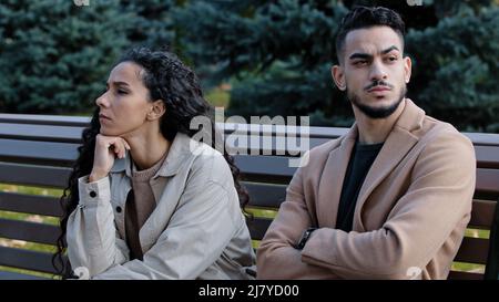 Un jeune couple hispanique offensé regardant dans une direction différente assis sur le banc dans le parc d'automne a énervé le silence mec indignant fille fortement soupir penser Banque D'Images