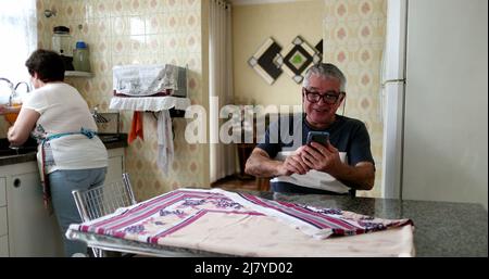 Joyeux senior commémorant les bonnes nouvelles sur le téléphone portable. Couple marié à la cuisine maison célébrant Banque D'Images