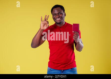 Beau jeune homme africain heureux Kenya Afrique touriste isolé mur jaune arrière-plan tenant des billets avec passeport et verre de queue de cotier voyage autour de la Banque D'Images