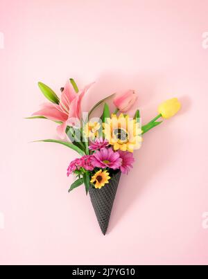 Un bouquet de Saint-Valentin ou de mariage de fleurs fraîches roses et jaunes de printemps dans une glace à cône. Concept de couleur pastel créative. Banque D'Images