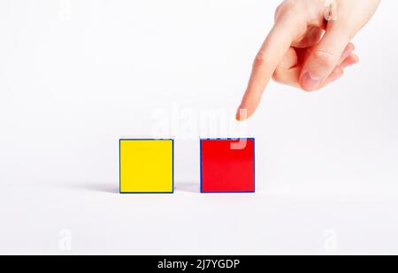 Concept de choix. Index pointant vers le cube rouge au lieu du cube jaune. Prise de décision entre deux variantes, propositions. Photo de haute qualité Banque D'Images